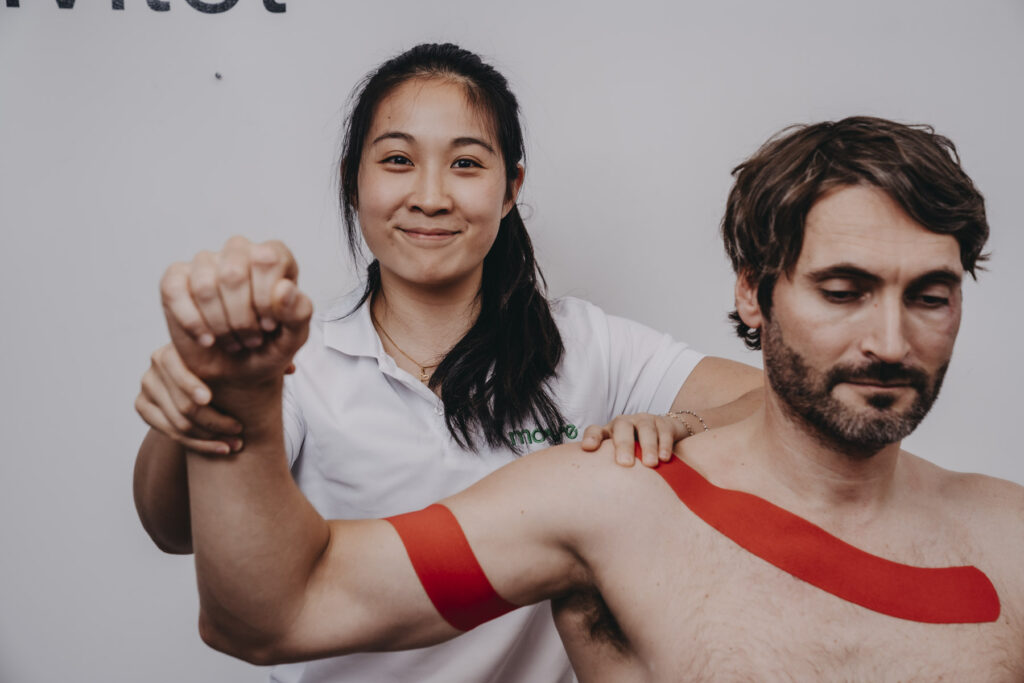 Kiropraktor Camelia Ong legger rød kinesiotape på skulderen og overarmen til en pasient