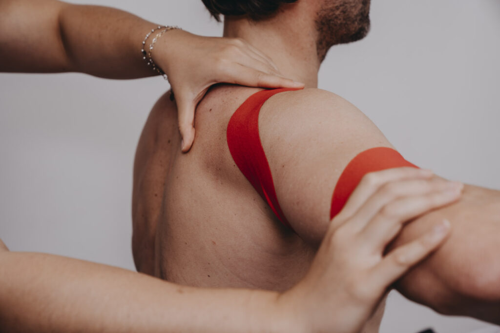 Nærbilde av rød kinesiotape som legges på skulderen til en pasient