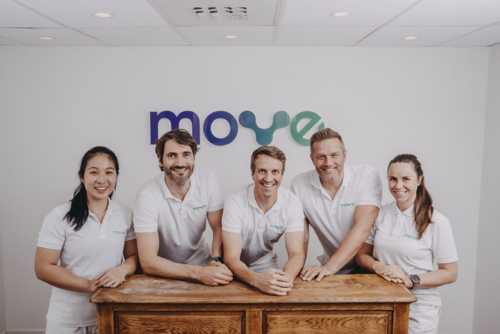 Fem behandlere hos Move kiropraktikk lener seg mot resepsjonsdisken under Move-logoen